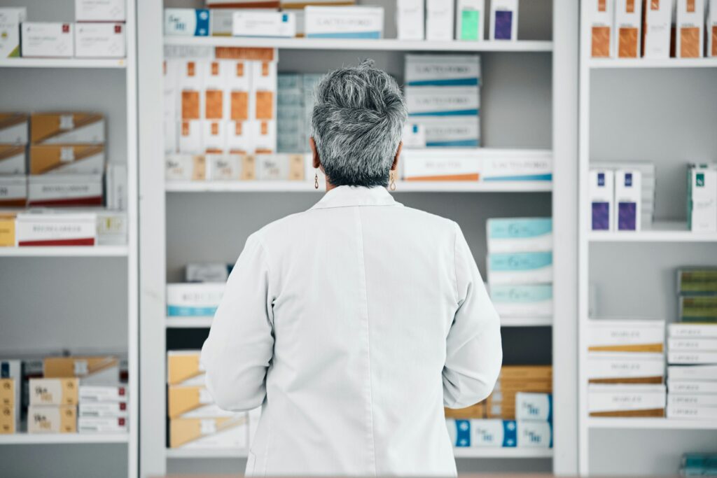 Stock, back and pharmacist at a medicine shelf for healthcare, medical work and service at a pharma